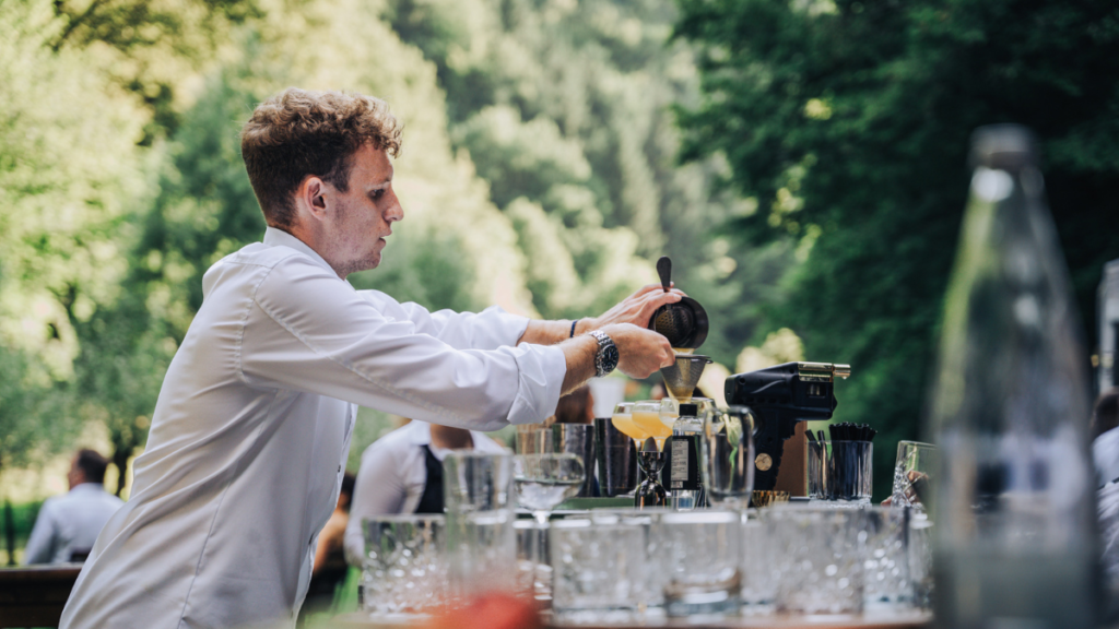 1️⃣ Alt Text:
"Profesionalni cocktail barman pripravlja svež koktajl na dogodku na prostem, pred občinstvom.